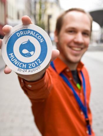 Florian Lorétan holds out the official DrupalCon Munich promotional beer coaster