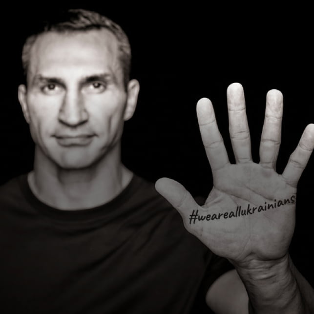 Man showing the palm of his hand to the camera. The palm has the tag #WeAreAllUkrainians