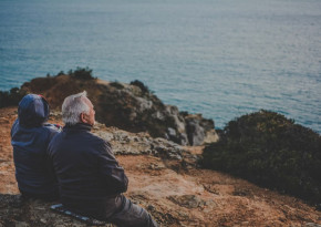 Elderly couple sitting on a cliff overseeing the sea