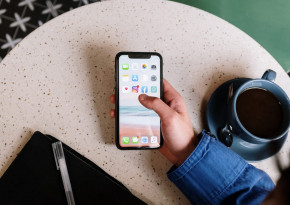 Image in the point of view of a user holding a mobile phone over a table next to a cup of coffee